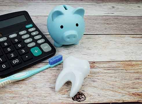 tooth and toothbrush next to a calculator and piggy bank on a wood countertop