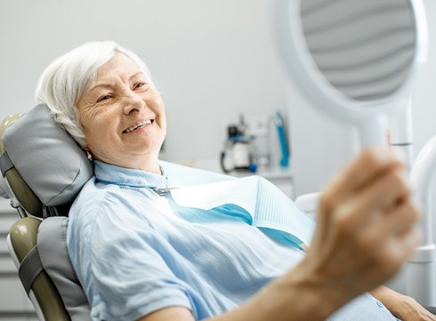Senior woman in dental chair looking at her smile in a mirror