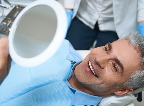 Man in dental chair looking at his smile in mirror