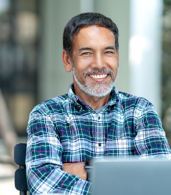 Senior man sitting at computer and smiling with arms folded