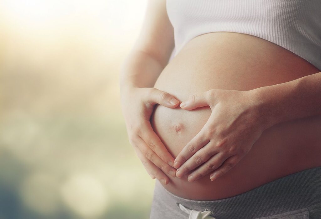 Woman making a heart with hands over her pregnant belly