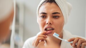Woman worriedly examining gums while brushing her teeth.